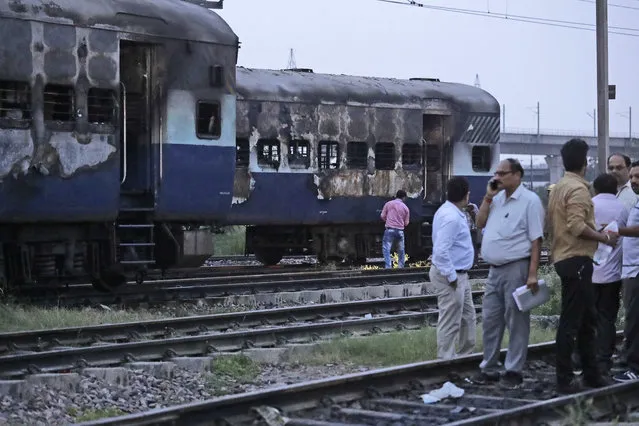 People stand near vandalized train coaches in New Delhi, India, Friday, August 25, 2017. Mobs rampaged across the north Indian town of Panchkula on Friday after a court declared a quasi-religious sect leader guilty of raping two of his followers. Two coaches of an empty train parked in New Delhi's Anand Vihar station were also set on fire. (Photo by Manish Swarup/AP Photo)