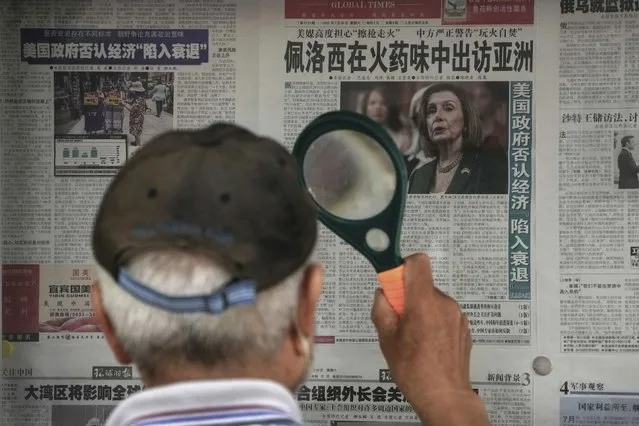 A man uses a magnifying glass to read a newspaper headline reporting on U.S. House Speaker Nancy Pelosi's Asia visit, at a stand in Beijing, Sunday, July 31, 2022. Pelosi, confirmed Sunday she will visit four Asian countries this week but made no mention of a possible stop in Taiwan that has fueled tension with Beijing, which claims the island democracy as its own territory. (Photo by Andy Wong/AP Photo)