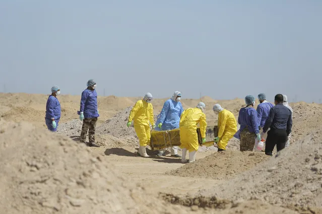 Iraqi health ministry workers carry a coffin of a person who died from coronavirus at a new cemetery for the people who died from Covid-19 outside the town of Najaf, Iraq, Monday, March 30, 2020. (Photo by Anmar Khalil/AP Photo)