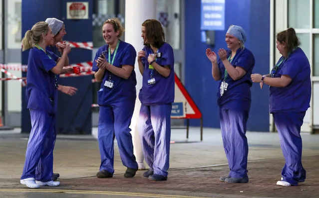Staff from the Royal Liverpool University Hospital join in a national applause to salute local heroes during the nationwide Clap for Carers NHS initiative to applaud workers fighting the coronavirus pandemic, Thursday, April 2, 2020, in Liverpool, England. (Photo by Peter Byrne/PA Wire via AP Photo)