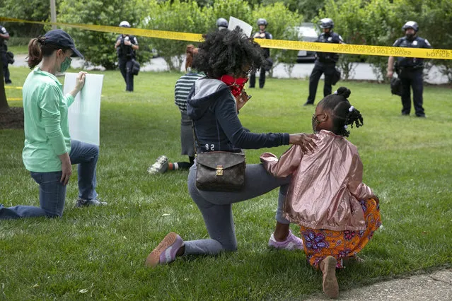 Ericka Ward-Audena, of Washington, puts her hand on her daughter Elle Ward-Audena, 7, as they take a knee in front of a police line during a protest of President Donald Trump's visit to the Saint John Paul II National Shrine, Tuesday, June 2, 2020, in Washington. “I wanted my daughter to see the protests, it's really important. I've gotten a million questions from her because of it”, says Ward-Audena, “I think the most egregious statement was 'when they start looting, we start shooting.' That crossed a line for me”. Protests continue over the death of George Floyd, who died after being restrained by Minneapolis police officers. (Photo by Jacquelyn Martin/AP Photo)