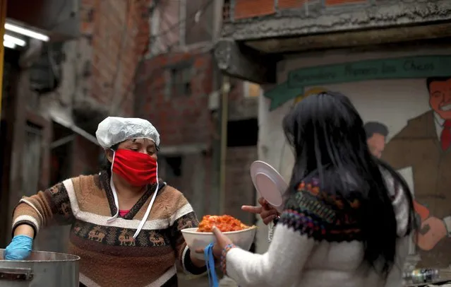 A volunteer serves free food to a resident inside the Fraga slum, during a government-ordered lockdown to curb the spread of the new coronavirus, in Buenos Aires, Argentina, Saturday, June 6, 2020. (Photo by Natacha Pisarenko/AP Photo)