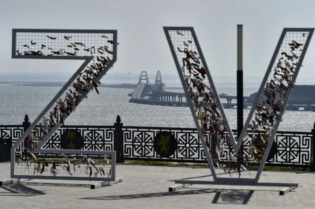 A helicopter dropping water to stop fire on Crimean Bridge connecting Russian mainland and Crimean peninsula over the Kerch Strait, is seen through the letters Z and V, which have become a symbol of the Russian military, in Kerch, Crimea, Saturday, October 8, 2022.. (Photo by AP Photo/Stringer)