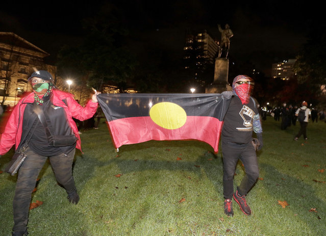 Protestoers carry an Aboriginal flag as the walk past a statue of British explorer James Cook in Sydney, Friday, June 12, 2020, to support U.S. protests over the death of George Floyd. Hundreds of police disrupted plans for a Black Lives Matter rally but protest organizers have vowed that other rallies will continue around Australia over the weekend despite warnings of the pandemic risk. (Photo by Rick Rycroft/AP Photo)