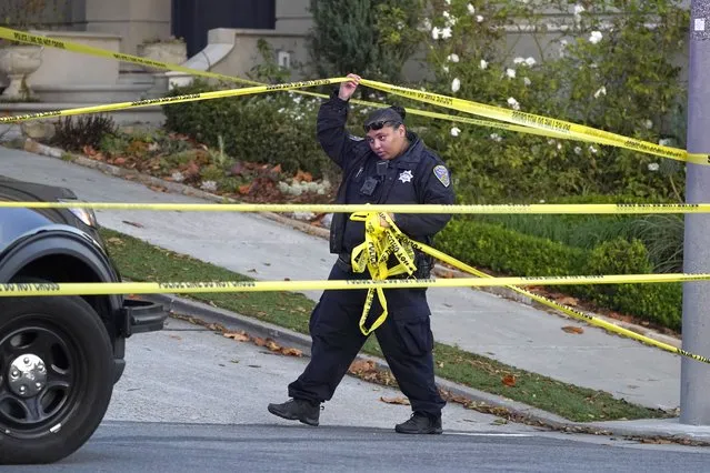 A police officer rolls out more yellow tape on the closed street below the home of Paul Pelosi, the husband of House Speaker Nancy Pelosi, in San Francisco, Friday, October 28, 2022. Paul Pelosi, was attacked and severely beaten by an assailant with a hammer who broke into their San Francisco home early Friday, according to people familiar with the investigation. (Photo by Eric Risberg/AP Photo)