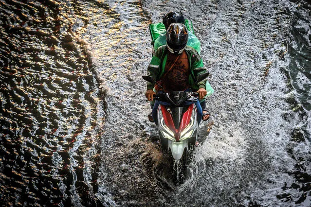 A couple rides a scooter on a street flooded due to heavy rain in downtown Bangkok on June 16, 2020. (Photo by Mladen Antonov/AFP Photo)