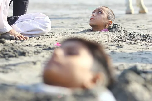 A disabled child is buried up to his neck in sand during the partial solar eclipse in belief its rays can heal, in Karachi, Pakistan, 25 October 202. A partial solar eclipse occurs when a portion of the Earth is engulfed by the shadow (penumbra) cast by the Moon as it passes between our planet and the Sun in imperfect alignment. During this eclipse - the first of the decade – the Moon appears to cover the Sun, leaving the Sun's halo as a visible rim forming an annulus, popularly known as the 'ring of fire. (Photo by Shahzaib Akber/EPA/EFE/Rex Features/Shutterstock)