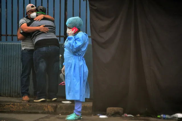 Relatives of an alleged COVID-19 victim embrace as a health worker speaks on the phone at a field hospital set up in the yard of the School Hospital in Tegucigalpa, on July 22, 2020. At least 1,000 have died and 30,867 have been infected with COVID-19 in Honduras, amid corruption accusations against Honduran President Juan Orlando Hernandez in the purchase of seven mobile hospitals, biosecurity equipment and material. (Photo by Orlando Sierra/AFP Photo)