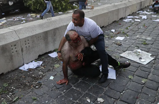 Lebanese man helps an injured man who was wounded by an explosion that hit the seaport, in Beirut Lebanon, Tuesday, August 4, 2020. (Photo by Hussein Malla/AP Photo)