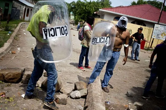 Masked miners and their family members, some holding police shields, patrol a road block they set up in their neighborhood in El Limon, Nicaragua, Wednesday, October 7, 2015. Clashes between police and miners erupted Tuesday when police tried to remove roadblocks set up all over town by miners who went on strike two weeks ago to protest the firing of several of their union members by the Canadian mine company B2Gold. According to police, one officer died in the violence. (Photo by Esteban Felix/AP Photo)
