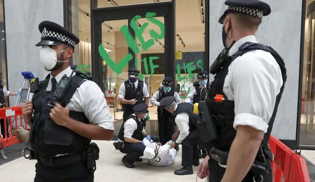 A climate protester is arrested by police after painting on the doors to the Shell oil company building in London, Friday, August 28, 2020. Climate protesters say they are holding a series of protests over the coming days to highlight climate change and environmental damage. (Photo by Alastair Grant/AP Photo)