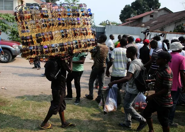 A sunglasses street salesman carries his wares as opposition supporters detain a man accused ofworking for a Congolese intelligence service in front of an opposition party Union for Democracy and Social Progress (UDPS) office in Kinshasa, Democratic Republic of Congo, September 23, 2016. (Photo by Goran Tomasevic/Reuters)