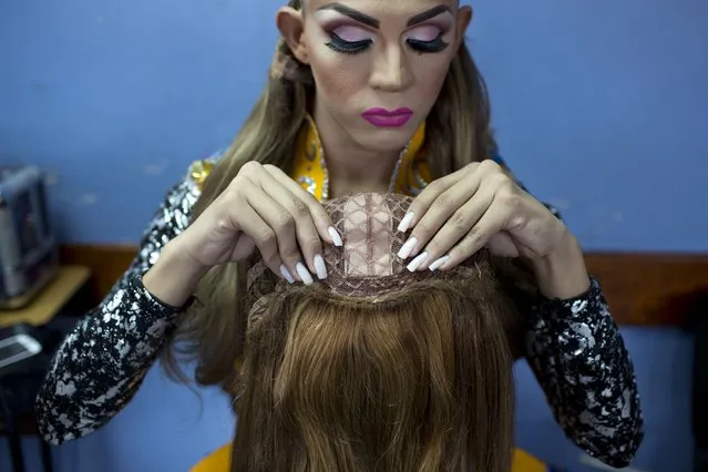 In this October 18, 2015 photo, contestant Jorge Solano, Miss Gay Cojedes, inspects his wig backstage at the ninth annual Miss Gay Venezuela beauty pageant in Caracas, Venezuela. Some contestants can afford to use wigs made of real, natural hair, while others use synthetic wigs. (Photo by Ariana Cubillos/AP Photo)