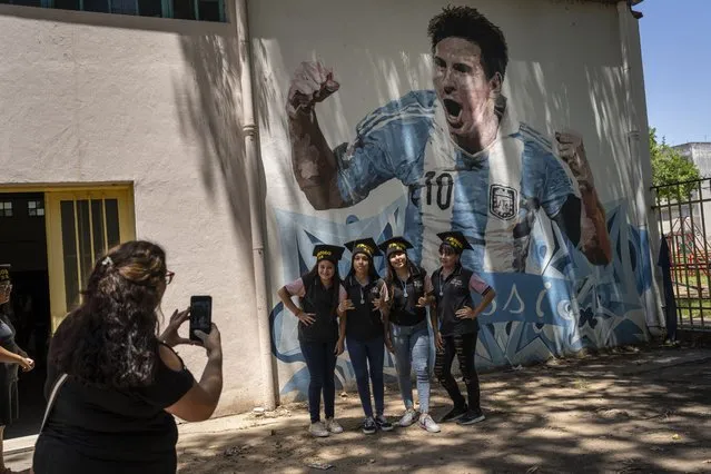 Students graduating from the General Las Heras elementary school, where Lionel Messi also attended school, pose for a group photo wearing their graduation hats by a mural of Messi, on the last day of school in Rosario, Argentina, Wednesday, December 14, 2022. (Photo by Rodrigo Abd/AP Photo)