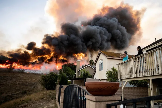 Inhabitants look at the flames from their homes rising form nearby hills as firefighters work at controlling the spread of the Blue Ridge Fire by lighting back fires near homes in Butterfield Ranch, Orange County, South of Los Angeles, California, USA, 27 October 2020. (Photo by Étienne Laurent/EPA/EFE)