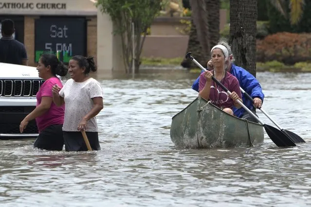 Residents paddle and walk along a flooded road Thursday, April 13, 2023, in Fort Lauderdale, Fla. Over two feet of rain fell causing widespread flooding, closing the Fort Lauderdale airport and turning thoroughfares into rivers. (Photo by Marta Lavandier/AP Photo)