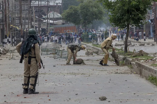 Indian policemen remove rocks, set up as barricade by Kashmiri protesters, near the site of a gun battle in Srinagar, Indian controlled Kashmir, Saturday, May 5, 2018. Fierce clashes erupted when residents in solidarity with the rebels tried to march to the gunbattle site. A vehicle belonging to Indian troops ran over and killed a man as protesters clashed with government forces, residents said. (Photo by Dar Yasin/AP Photo)