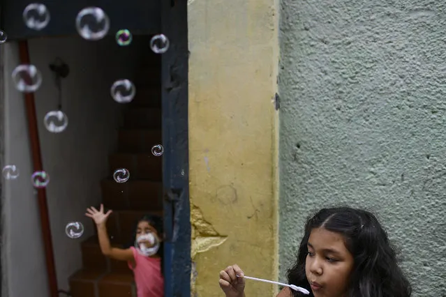 A girl plays with soap bubbles with her sister at the Catia neighborhood on Christmas Day in Caracas, Venezuela, Friday, December 25, 2020, amid the new coronavirus pandemic. (Photo by Matias Delacroix/AP Photo)