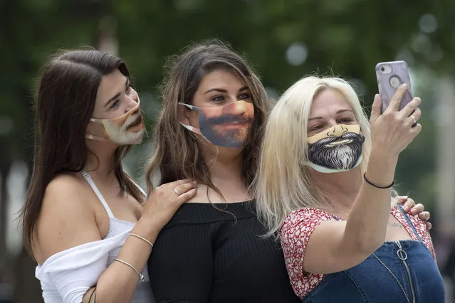 Three women wearing novelty masks with beard prints take a selfie on Queen Street on August 4, 2020 in Cardiff, United Kingdom. Coronavirus lockdown measures continue to be eased as the number of excess deaths in Wales falls below the five-year average. From this week up to 30 people can meet outdoors and pubs, restaurants and cafes can open to customers indoors. (Photo by Matthew Horwood/Getty Images)