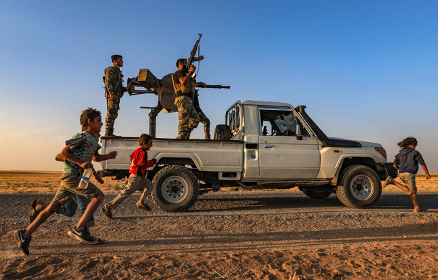 Children run past a gun-mounted truck manned by Turkey-backed Syrian fighters near the rebel-controlled town of Tal Abyad in the northern Syria's Raqa province, along the frontline with Syrian Kurdish forces controling the Kurdish-majority city of Kobani, on October 10, 2020. (Photo by Bakr Alkasem/AFP Photo)
