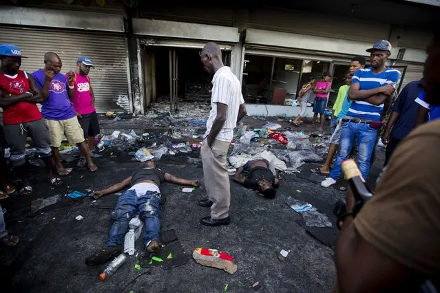 The bodies of two men lie outside a burned and looted store, as one of the men's relatives stands between them, after two days of protests against a planned hike in fuel prices in Port-au-Prince, Haiti, Sunday, July 8, 2018. Government officials had agreed to reduce subsidies for fuel as part of an assistance package with the International Monetary Fund, but the government suspended the fuel hike after widespread violence broke out. (Photo by Dieu Nalio Chery/AP Photo)