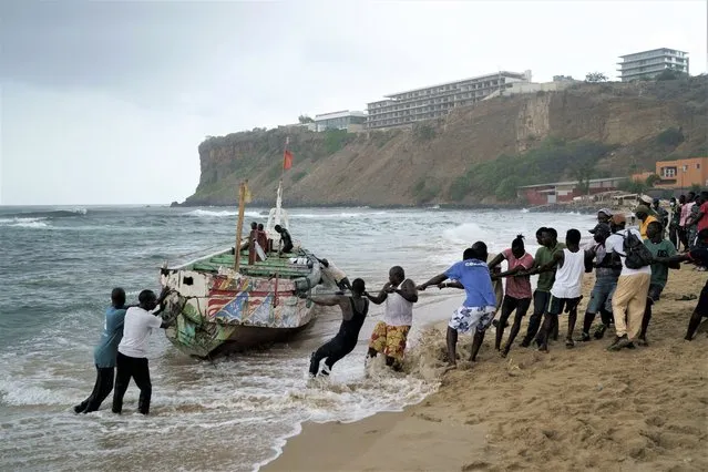 People work together to pull, according to the locals, the capsized boat ashore at the beach where several people were found dead in Dakar, Senegal, Monday, July 24, 2023. The bodies were discovered by the navy early in the morning and are believed to be migrants because of the type of boat they were in according to the authorities. (Photo by Leo Correa/AP Photo)