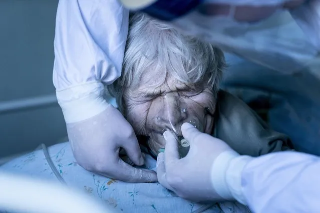 A medic wearing a special suit against coronavirus adjusts a coronavirus patient's oxygen mask at the intensive care unit at a hospital in the mining town of Selydove, 700 kilometers (420 miles) east of Kyiv, eastern Ukraine, Thursday, March 4, 2021. (Photo by Evgeniy Maloletka/AP Photo)