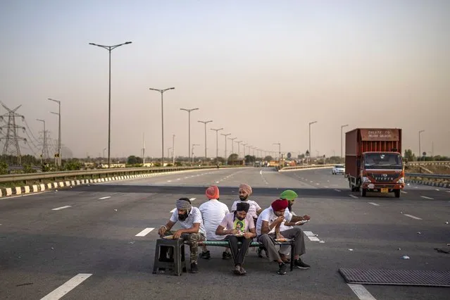 Farmers eat a meal on a cot during a 24-hour blockade of a major expressway as part of their ongoing protests against new farm laws in Dasna, India, Saturday, April 10, 2021. (Photo by Altaf Qadri/AP Photo)