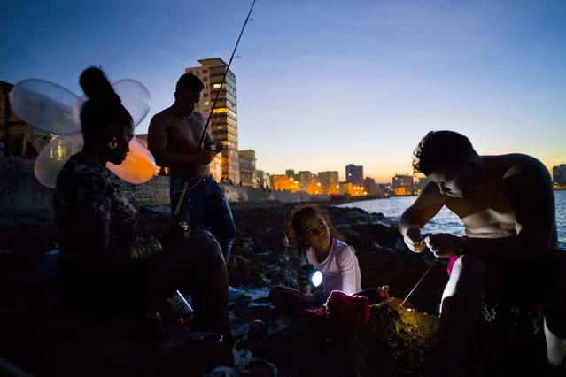 In this November 13, 2016 photo, Edelmis Ferro Solano, far left, holds inflated condoms for her husband Junior Torres Lopez, standing behind her, to use on his fishing line as a bobber, while her granddaughter Leyanis Macias Puente helps out by shining a flashlight on the hook of family friend Fran Luis Martinez Nueva, as they fish along the malecon seawall in Havana, Cuba. According to the fishermen’s lore, the inventor of the balloon technique in Cuba saw a video of South Africans fishing using kites and got the idea for using inflated condoms. (Photo by Ramon Espinosa/AP Photo)