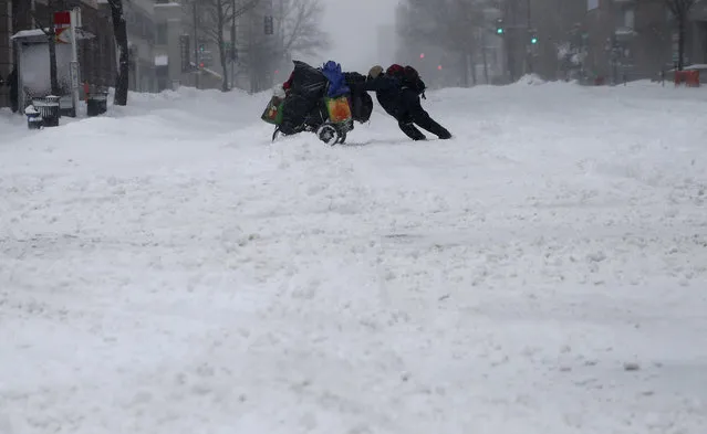 A homeless man pushes a cart with his belongings across 13th Street in downtown Washington, Saturday, January 23, 2016. Millions of people awoke Saturday to heavy snow outside their doorsteps, strong winds that threatened to increase through the weekend, and largely empty roads as residents from the South to the Northeast heeded warnings to hunker down inside while a mammoth storm barreled across a large swath of the country. (Photo by Gerald Herbert/AP Photo)