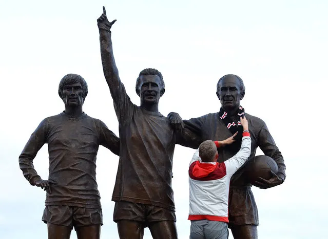 A football fan ties a scarf around a statue of Manchester United and England star Bobby Charlton outside the club's Old Trafford stadium on October 21, 2023 following his death at the age of 86. (Photo by Carl Recine/Reuters)