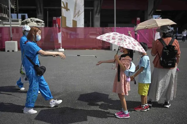 A volunteer sprays water on children as they use umbrellas to beat the heat outside the Fuji International Speedway, the finish for the women's cycling road race that is underway, at the 2020 Summer Olympics, Sunday, July 25, 2021, in Oyama, Japan. (Photo by Christophe Ena/AP Photo)