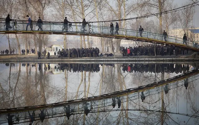 In this Friday, January 6, 2017 photo, pedestrians and cyclists are reflected in the Pothong River as they cross a bridge at the start of their work day in Pyongyang, North Korea. (Photo by Wong Maye-E/AP Photo)