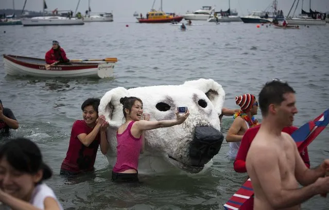 People pose next to a polar bear costume worn by two participants in English Bay during the 94th annual New Year's Day Polar Bear Swim in Vancouver, British Columbia on January 1, 2014. (Photo by Ben Nelms/Reuters)