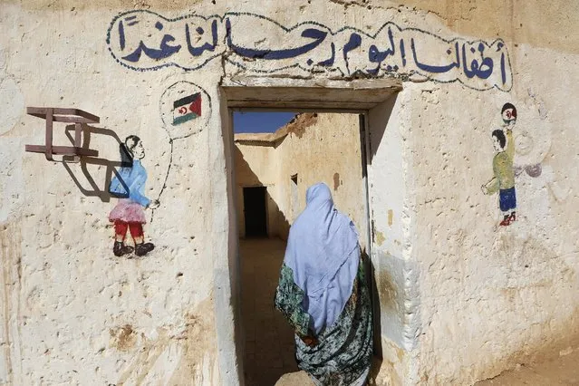 An indigenous Sahrawi woman walks into a nursery in a refugee camp of Boudjdour in Tindouf, southern Algeria March 3, 2016. The writing in Arabic reads: “Our children of today are our future men”. (Photo by Zohra Bensemra/Reuters)