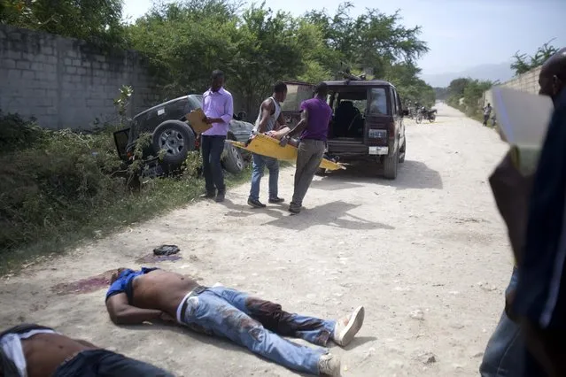 Morgue workers carry a woman's body to their vehicle at a crime scene where two other men were also found dead in Tabarre, a town on the outskirts of Port-au-Prince, Haiti, early Friday, May 1, 2015. Investigators removed three bodies, found handcuffed and blindfolded, from a car, far left, parked on the side of a street surrounded by open land and about three blocks from the U.S. embassy. (Photo by Dieu Nalio Chery/AP Photo)