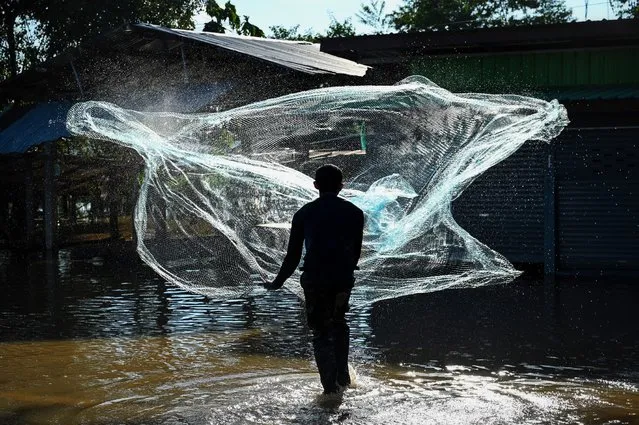 A resident casts a net to go fishing in his partially submerged village in the central Thai province of Lopburi on September 28, 2021, as tropical storm Dianmu caused flooding in 30 provinces across the country. (Photo by Lillian Suwanrumpha/AFP Photo)