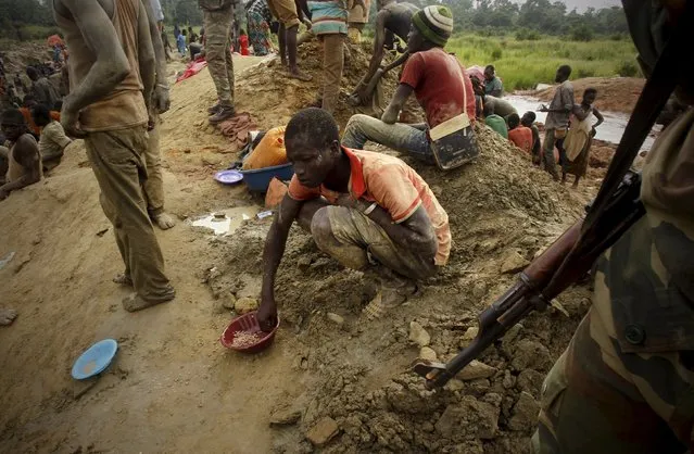 A gold prospector sits and eats close to a soldier at a gold mine near the village of Gamina, in western Ivory Coast, March 18, 2015. (Photo by Luc Gnago/Reuters)