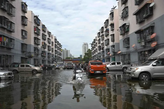 A resident drives through flooded housing estates in Khlong Toey district as water from the Chao Praya River floods low lying areas in Bangkok on November 10, 2021. (Photo by Lillian Suwanrumpha/AFP Photo)
