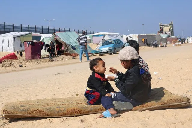 Displaced Palestinian girl, who fled her house due to Israeli strikes, feeds her brother at a tent camp, near the border with Egypt, in Rafah in the southern Gaza Strip, on February 25, 2024. (Photo by Saleh Salem/Reuters)