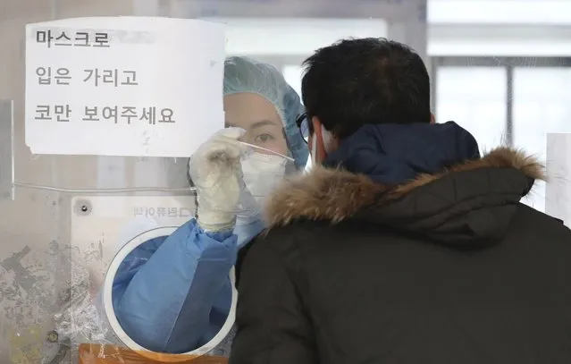 A medical worker wearing protective gear in a booth, takes sample from a man at a temporary screening clinic for the coronavirus in Seoul, South Korea, Saturday, December 4, 2021. South Korea again broke its daily records for coronavirus infections and deaths and confirmed three more cases of the new omicron variant as officials scramble to tighten social distancing and border controls. (Photo by Park Mi-so/Newsis via AP Photo)