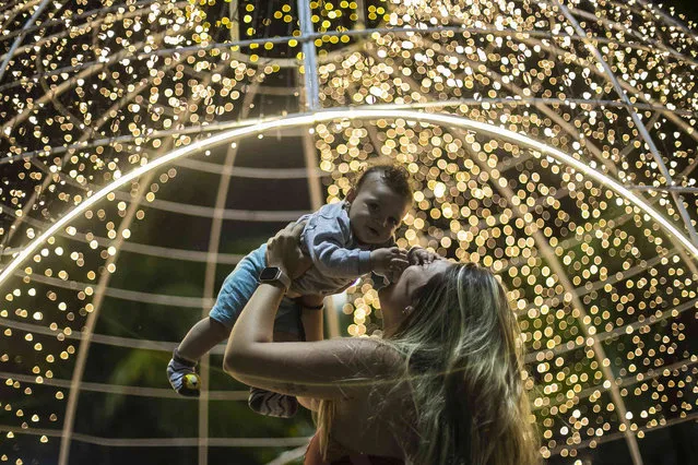 A woman lifts a baby in front of holidays lights during a Christmas celebration along Copacabana beach, in Rio de Janeiro, Brazil, Saturday, December 11, 2021. (Photo by Bruna Prado/AP Photo)
