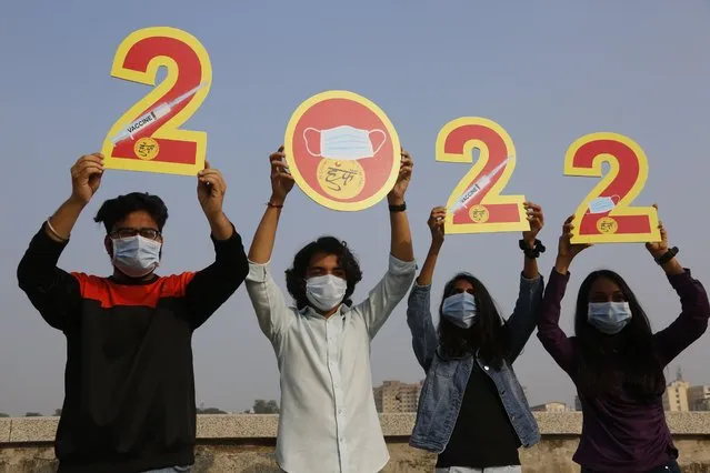 Indians, wearing face masks to help curb the spread of the coronavirus, hold the cutouts to welcome 2022 on New Year’s Eve in Ahmedabad, India, Friday, December 31, 2021. (Photo by Ajit Solanki/AP Photo)
