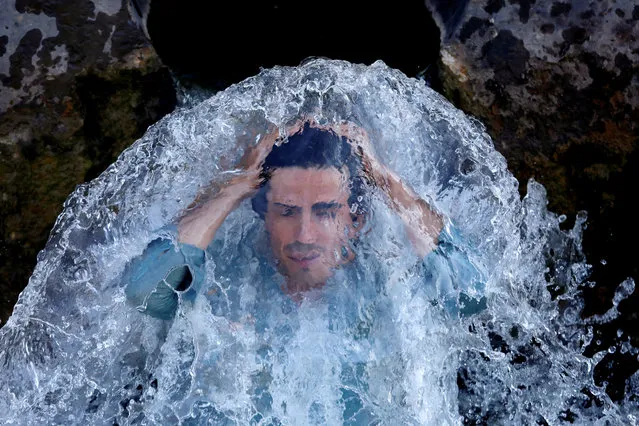 A man cools off under a water pipe from a canal on the outskirts of Peshawar, Pakistan on June 13, 2019. (Photo by Fayaz Aziz/Reuters)