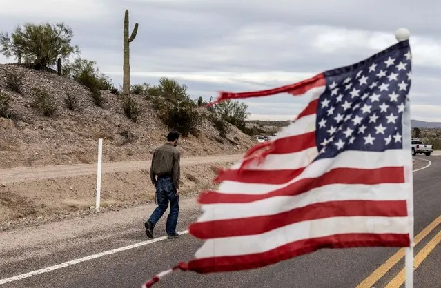 A tattered U.S. flag is pictured as a man walks down a road while supporters of former U.S. president Donald Trump attend a rally in Florence, Arizona, U.S., January 15, 2022. (Photo by Carlos Barria/Reuters)