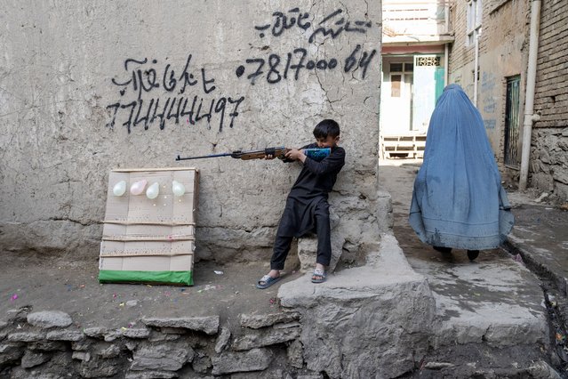 An Afghan burqa-clad woman (R) walks past a boy carrying an airgun in Kabul on March 24, 2024. (Photo by Wakil Kohsar/AFP Photo)