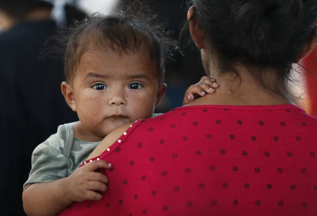 A Honduran migrant mother and her 7-month-old child stand in line to board a bus that will take them and other migrants to Monterrey, from an immigration center in Nuevo Laredo, Mexico, Thursday, July 18, 2019. The migrants have been returned by authorities from the U.S. and are bused to the Mexican city of Monterrey under their own recognizance. (Photo by Marco Ugarte/AP Photo)