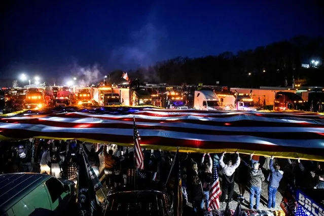 People hold up a giant American flag while hundreds of vehicles including 18-wheeler trucks, RVs and other cars are parked as part of a rally at Hagerstown Speedway after some of them arrived as part of a convoy that traveled across the country headed to Washington D.C. to protest coronavirus disease (COVID-19) related mandates and other issues in Hagerstown, Maryland, U.S., March 5, 2022. (Photo by Stephanie Keith/Reuters)