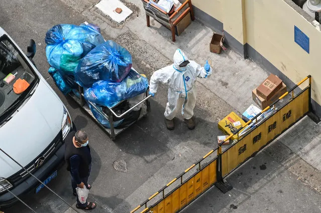A worker wearing personal protective equipment (PPE) pulling a cart with bags stands at a checkpoint during a Covid-19 coronavirus lockdown in the Jing'an district in Shanghai on April 20, 2022. (Photo by Hector Retamal/AFP Photo)