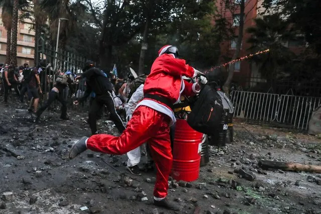 A demonstrator in Santa Claus outfit tosses a rock at security forces during a protest against Chile's government in Santiago, Chile on December 13, 2019. (Photo by Ivan Alvarado/Reuters)